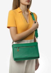 Borsa a tracolla in pelle verde con tasca frontale con zip, forma rettangolare, tracolla rimovibile e dettaglio con etichetta dorata.