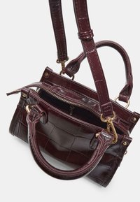 Mal�á tmavě burgundská kabelka s krokodýlí strukturou, zlatými kovovými prvky, zapínáním na zip, dvěma uchy a nastavitelným ramenním popruhem.
