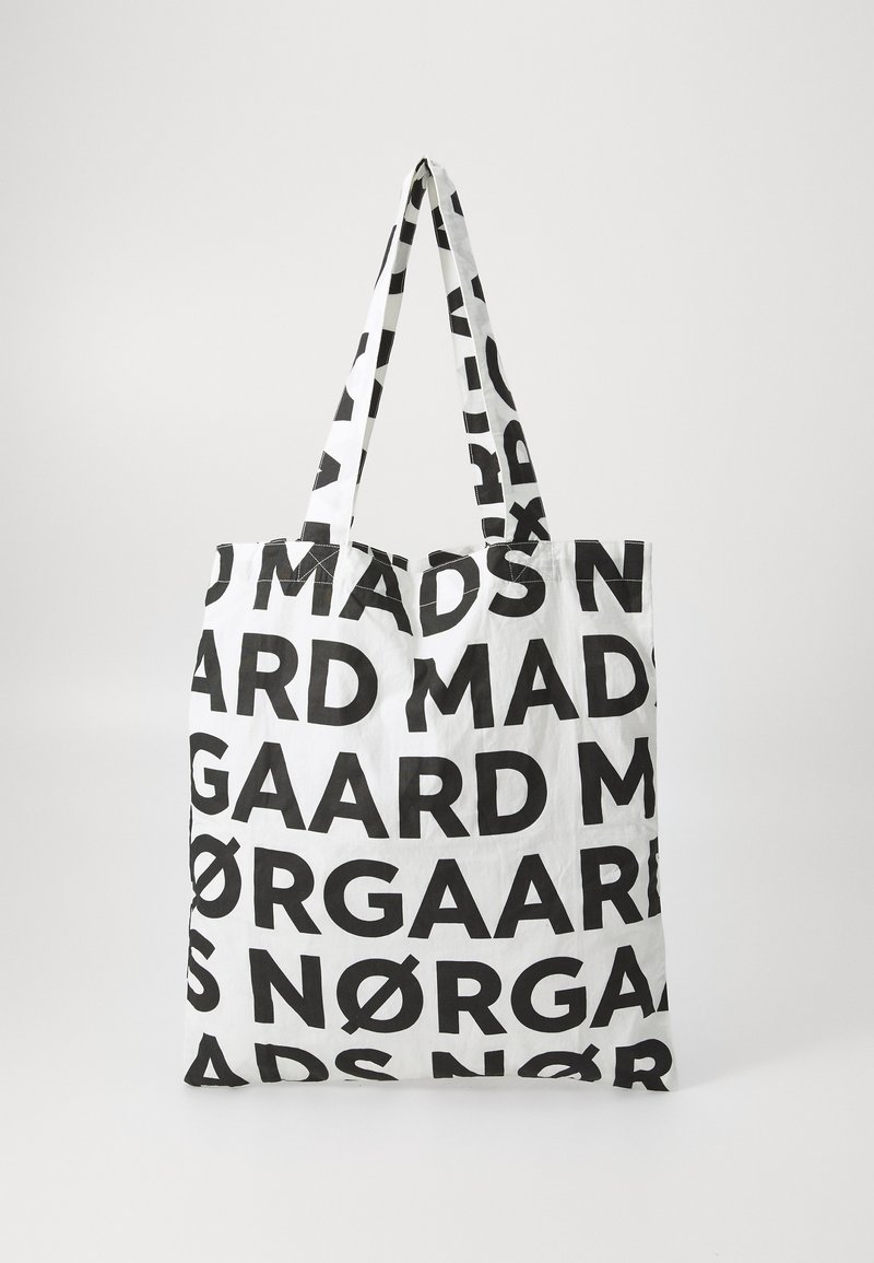 Veľká biela taška na rameno s výrazným, opakujúcim sa čiernym textom so slovami "MADS NØRGAARD." Navrhnutá s dvoma pevným popruhmi. Ľahká tkanina.