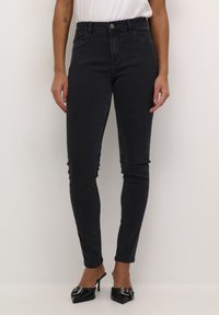 Jean skinny noir taille haute en denim avec cinq poches, des coutures décoratives et une fermeture à bouton argenté. Silhouette ajustée et longueur chevilles.