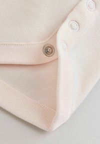 Zbliżenie na jasnoróżowy materiał z metalowym zatrzaskiem i naszytymi dziurkami na guziki wzdłuż krawędzi do zapinania.