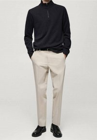 Pullover nero a maglia con colletto a mezza zip, abbinato a pantaloni beige su misura e scarpe di pelle nere. Design semplice e colori neutri.