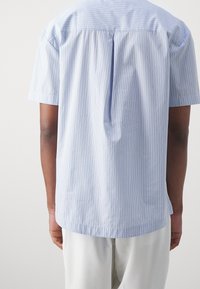 Lyhythihainen paita vaaleansinisellä värillä, jossa on pystysuorat valkoiset raidat. Ominaisuuksiin kuuluu rento istuvuus ja keskelle selkään sijoitettu poikkisauma. Materiaali puuvillasekoitetta.