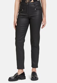 Černé přiléhavé kalhoty s hladkou texturou, které mají dvě přední kapsy na zip a zapínání na knoflík v pase. Úzký střih nohavic.
