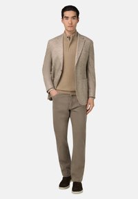 Beige houndstooth-blazer över en tanstickad polo och ljusbruna byxor, i kombination med mörkbruna mockaskor; minimalistisk design, skräddarsydd passform.