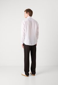Camisa de lino blanca ligera con mangas largas, cuello pequeño y dobladillo curvado, combinada con pantalones negros y zapatillas blancas.