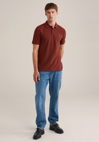 Rød polo skjorte med et lille logo på brystet, parret med lyseblå straight-leg jeans og sorte sko. Simpelt, casual design.