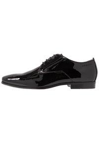 Scarpa da uomo nera in vernice con punta affusolata, cinque occhielli e design minimalista, dotata di suola in gomma e logo del brand sottile.