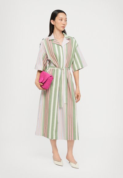 Robe rayée avec des lignes verticales vertes, roses et blanches ; manches courtes ; taille ceinturée ; modèle tenant une pochette texturée rose ; chaussures beiges à talons pointus.