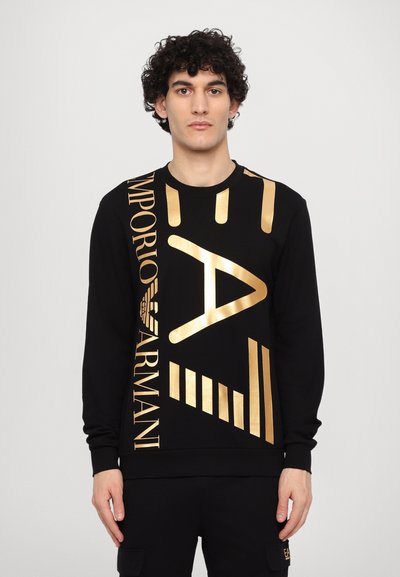 Sweatshirt noir en coton, avec un logo doré imprimé et des motifs géométriques sur le devant. Manches longues avec des poignets côtelés.