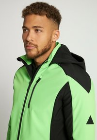 Green and black hooded jacket with a zippered front, made of soft fabric, featuring angular black panels and a logo accent on the sleeve.