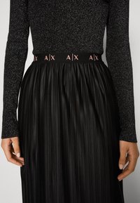 Černá plisovaná sukně s texturovaným povrchem, s kontrastním elastickým pasem s růžovým logem "AX". Dlouhý rukáv s třpytivým efektem.