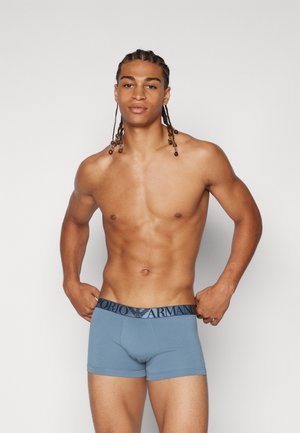 Hellblaues Boxershorts mit einem schwarzen Logo-Bund. Der Stoff ist glatt und hat ein enganliegendes Design, das die Körperhaltung des Trägers betont.