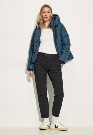 Doudoune bleue à capuche avec une texture matelassée, haut à manches longues blanc, pantalon cargo noir et baskets blanches avec des accents noirs.