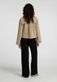 Beige kort jacka med långa ärmar, med sömnadsdetaljer på axlarna och en avslappnad passform, kombinerad med svarta vida byxor.