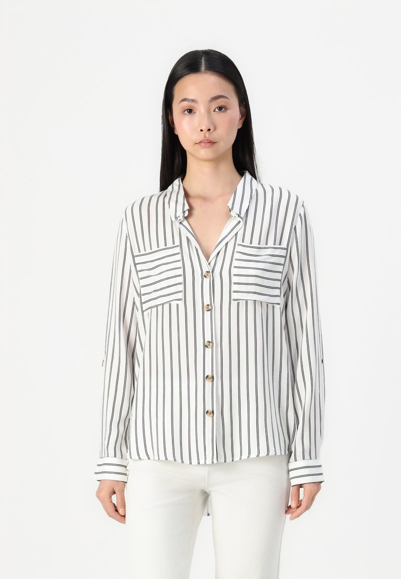 White button-up shirt with vertical black stripes, two chest pockets, and a collar. Long sleeves feature striped cuffs.