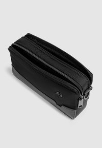 Bustina in tessuto nero con due scomparti con cerniera, una sezione inferiore liscia e un piccolo logo. Presenta una forma rettangolare e un design resistente.