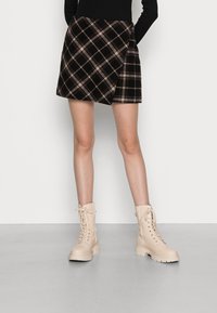 Sukně s kostkovaným vzorem v tmavých tónech s překládaným designem. Nošena s béžovými šněrovacími botami s robustní podrážkou a detaily na zip.