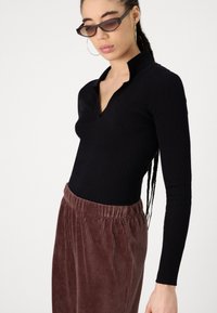 Μαύρη ριμπ μπλούζα με μακρύ μανίκι και γιακά σε σχήμα V, σε συνδυασμό με καφέ παντελόνι καδένιας, που διαθέτει ελαστική μέση.