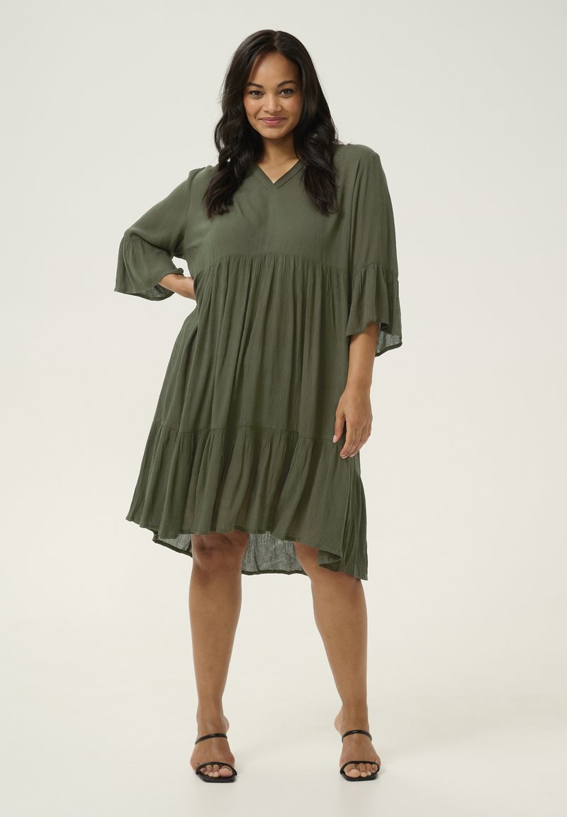 Vestido verde oliva de capas, hecho de una tela ligera, con escote en V, mangas de campana de tres cuartos y un dobladillo desigual.