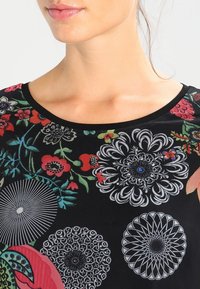 Schwarzes Blumenoberteil mit kunstvollen mehrfarbigen Drucken, darunter rote und blaue Blumen, rundem Ausschnitt und weichem Stoffgefühl.