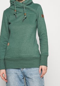 Felpa verde con collo a scialle e stringhe, caratterizzata da un tessuto testurizzato, polsini a costine e dettagli con pannelli laterali.