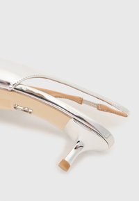 Chaussure à talon haut en cuir verni argenté avec une conception échancrée, bout rond et petit talon carré. Intérieur beige avec un minimum de détails.
