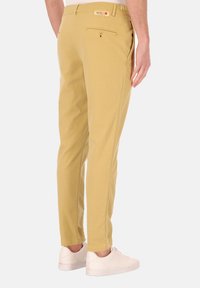 Licht kaki broeken met een slim fit, voorzien van een knoopzak aan de achterkant, subtiele stiksels en gecombineerd met witte sneakers.