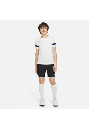 Nike jeugd sportkleding met een witte T-shirt met korte mouwen en marineblauwe strepen, zwarte shorts en witte kniekousen, met logokleuraccenten.
