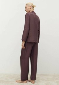 Set di abbigliamento da casa in malva composto da una camicia a maniche lunghe con colletto e pantaloni a gamba larga. Il tessuto ha una consistenza liscia e una vestibilità comoda.