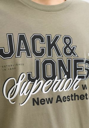 Close-up of beige shirt with bold black and white text "JACK & JONES Superior New Aesthetic" printed on fabric.