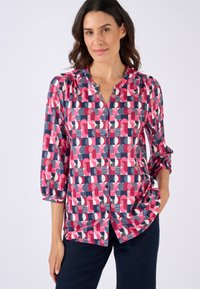 Blusa colorida con un estampado geométrico en rosa, azul marino y blanco. Tiene un cierre frontal con botones, mangas de tres cuartos y un corte holgado.