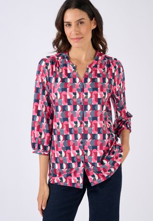 Blusa colorata con stampa geometrica in rosa, blu navy e bianco. Presenta una chiusura con bottoni, maniche a tre quarti e una vestibilità rilassata.
