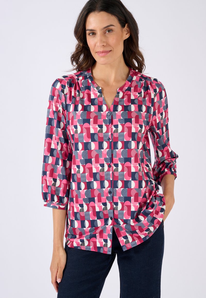 Blusa colorida con un estampado geométrico en rosa, azul marino y blanco. Tiene un cierre frontal con botones, mangas de tres cuartos y un corte holgado.