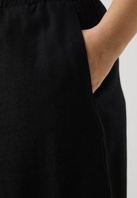Jupe noire tissée avec poches latérales, taille élastique et texture lisse. Le tissu présente des variations subtiles.