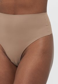 Woman wearing high-waisted seamless nude underwear, showing smooth fabric and clean edge stitching on dark skin tone.