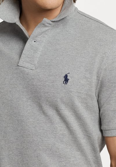 Gray polo shirt made of textured fabric, featuring a collared neckline and a small navy embroidered logo on the left chest.