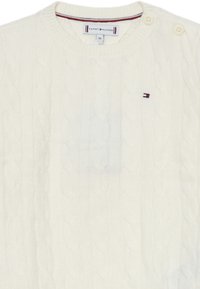 Maglione bianco a trecce con collo rotondo e due bottoni sulla spalla sinistra. Presenta un piccolo logo multicolore sul petto.