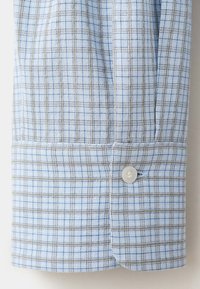 Close-up of a light blue and gray checkered shirt cuff with a single white button fastened.