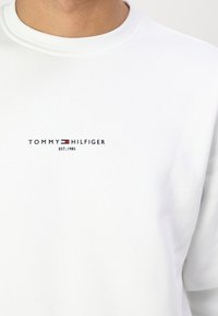 Biała bluza z bawełny z domieszką, z okrągłym dekoltem i logo z napisem "TOMMY HILFIGER" w kolorze czarnym i czerwonym. Gładka faktura.