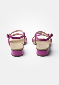 Fuchsia värisiä remmikenkiä, joissa on matala lohkoheel, kiiltävä materiaali, säädettävä solki ja sileä tan-värinen pohja.