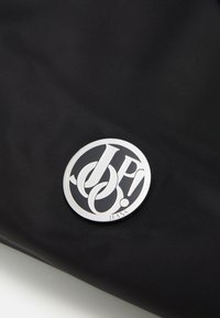 Borsa in tessuto nera con un logo circolare argentato con le lettere intrecciate "JP" e "JEANS" in basso, su uno sfondo texturizzato.