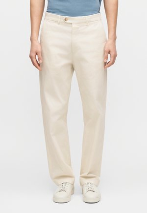 Beige bomuldsbukser med direkte ben, der har knaplukning og sidelommer, kombineret med hvide sneakers.