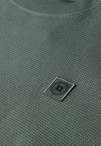 Felpa grigia con trama strutturata e motivo a rete traspirante, con patch logo cucito nell'angolo inferiore, scollo rotondo.