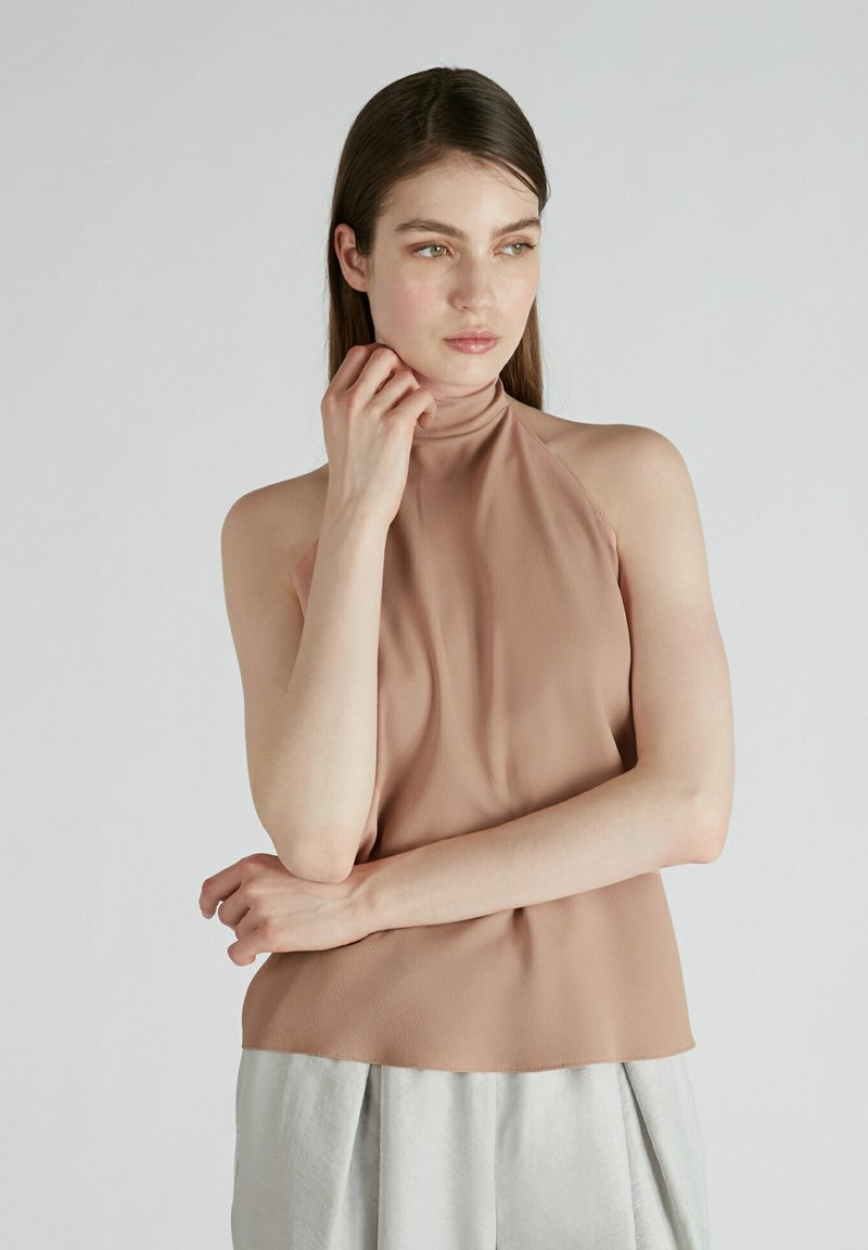 Top a collo alto di colore beige chiaro, realizzato in tessuto morbido con una texture liscia. Presenta una vestibilità rilassata e un design drappeggiato.