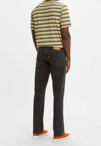 Pruhované tričko s krátkým rukávem v zelené a žluté barvě, doplněné o černé džíny a oranžové tenisky. Na zadní straně džín je štítek.