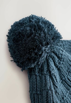 Dunkelblauer Strickmütze mit einem großen, strukturierten Pom-Pom oben, mit einem Kabelmuster im gesamten Körper. Weiches, dickes Material.