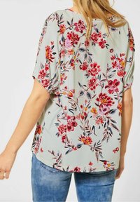 Blommig blus i ljusgrön tyg med korta puffärmar, med röda, rosa och blå blommönster på baksidan. Avslappnad passform.