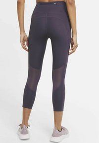 Leggings capri en violet foncé avec des panneaux en maille sur les côtés, taille haute et coutures contrastantes ; associés à des baskets violet clair.