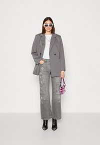 Grå oversized kavaj, vit topp, mönstrade grå jeans med paljetter, svarta spetsiga stövlar, rosa handväska och vita solglasögon.